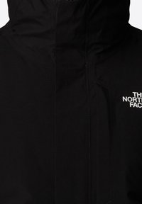 Schwarze wasserdichte Jacke mit hohem Kragen, Frontreißverschluss und Logoakzent. Glatte Textur mit matter Oberfläche und versiegelten Nähten.