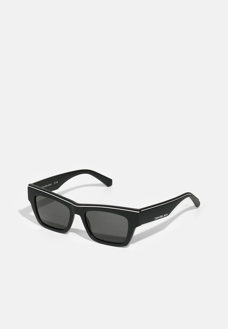 Gafas de sol negras con acabado mate, forma rectangular y lentes oscuros. Presentan un delgado acento blanco a lo largo del marco superior.