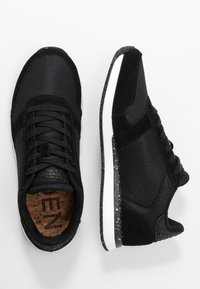 Black athletic shoes featuring a mesh and suede upper, textured accents, white midsole, and a speckled black outsole. Lace-up design.