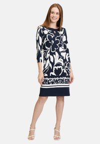Marinekleid mit weißem Blumenmuster, drei Viertelärmel, runder Ausschnitt mit Schlitzdetail und Streifen am Saum. Glatte Textur.