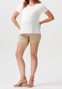 T-shirt bianco a maniche corte abbinato a pantaloni corti beige con risvolto, caratterizzato da una vestibilità comoda. Accessoriato con sandali con zeppa color cuoio chiaro.