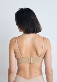 Beige bh med justerbare stropper, baklukking og glatt tekstur. Designet fremhever enkelhet og funksjonalitet.