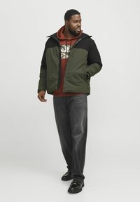 Groene en zwarte gewatteerde jas met rits. Gecombineerd met een bordeauxrode hoodie en een donkere spijkerbroek. Zwarte schoenen maken de outfit compleet.