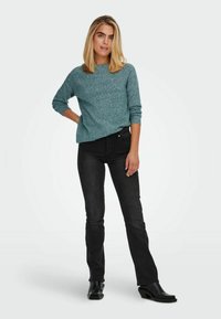 Maglione turchese a maglia con scollo rotondo e maniche lunghe, abbinato a jeans neri aderenti e stivaletti neri. Design semplice e moderno.