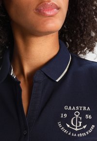 Polo shirt navy avec col, munit d'une bande argentée, logo brodé sur la poitrine et manches courtes en tissu coton texturé.