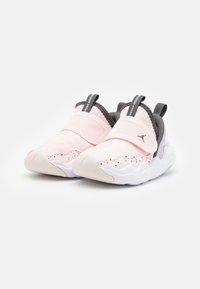 Světlé růžové tenisky na slip-on s černými skvrnami, bílými vlnovitými podrážkami, černými poutky na patě a černým logem Jumpman na pásku.