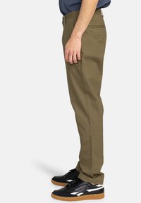 Olive green cotton chinos, straight-leg design, subtle crease details, side pockets, worn with black sneakers featuring white accents.