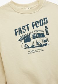 Beżowa bluza z kapturem z navy blue grafiką przedstawiającą food trucka. Tekst zawiera "FAST FOOD RIDER" oraz dodatkowe hasła poniżej. Miękka mieszanka bawełny.