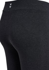 Zbliżenie ciemnoszarych dopasowanych legginsów z wysokim stanem i dwoma małymi białymi logo szewron w pobliżu góry.