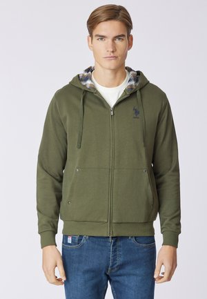 Felpa con zip verde oliva, cappuccio foderato a scacchi, tasche frontali con chiusura a scatto e un logo discreto sul petto. Materiale in cotone morbido.