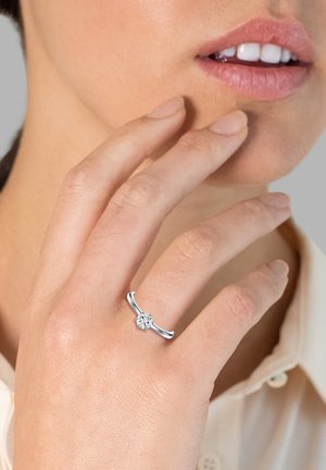 Silberring mit floralem Design, ausgestattet mit einem zentralen klaren Stein; glatte Band mit polierter Oberfläche, getragen an der Hand einer Person.