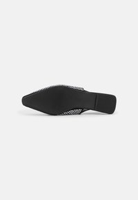 Zapato negro de malla sin cordones con punta afilada y tacón bajo, que presenta una suela de goma texturizada y un patrón recortado a lo largo de los lados.