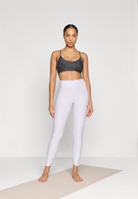 Sport-BH in Schwarz mit dünnen Trägern, kombiniert mit helllila Leggings mit hoher Taille und Seitentaschen. Glatte Textur, taillierte Passform.