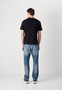 Tricou negru cu mânecă scurtă, asortat cu blugi din denim de culoare albastră deschisă, cu o croială lejeră și cusături vizibile pe buzunarele din spate.