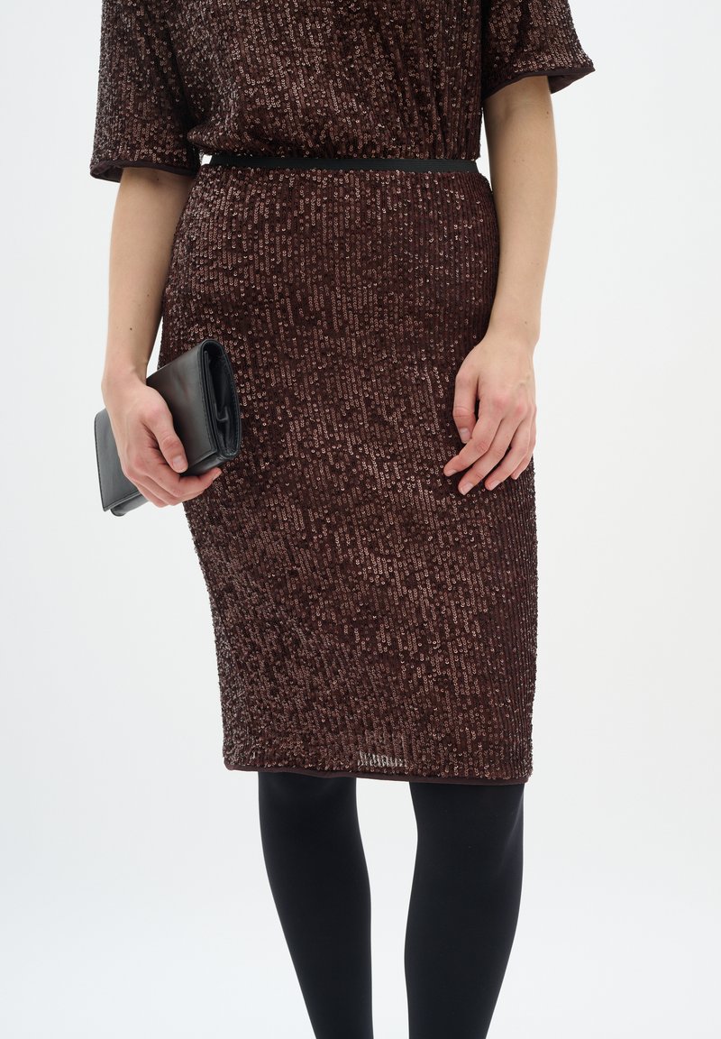 Brūns sekvencēts kleita ar pieguļošu siluetu, īsām piedurknēm, jostotu vidukli, apvienota ar melnu clutch somu un necaurspīdīgām melnām zeķbiksēm.
