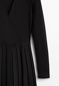 Robe noire avec un haut ajusté à côtes et une jupe plissée. Manches longues, décolleté en V, et texture de tissu lisse sur l'ensemble.