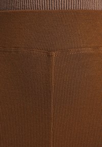 Gros plan d'un tissu tricoté côtelé marron avec des coutures visibles formant une couture et un détail de ceinture.