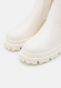 Stivaletti bianchi alla caviglia con una texture liscia, punta rotonda e suola spessa e texturizzata. Presentano pannelli laterali elasticizzati per una facile vestibilità.