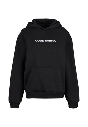 Svart hettegenser laget av myk fabric med kengurulomme, ribbestrikkede mansjetter og «GOOD KARMA» trykket i hvitt over brystet.