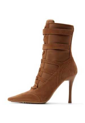 Brun ruskinds ankelstøvle med høj hæl, spids tå, fem vandrette remme og en slank stilethæle på hvid baggrund.