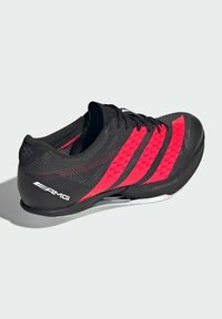Sort sportssko med røde detaljer har et strømlinet design, tekstureret overdel, snørebåndslukning og en let sål mærket "LIGHTSTRIKE PRO."