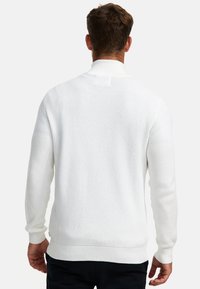 Suéter blanco de punto con un patrón texturizado, cuello alto y puños y dobladillo acanalados. La vista trasera muestra una construcción sin costuras y un detalle mínimo.
