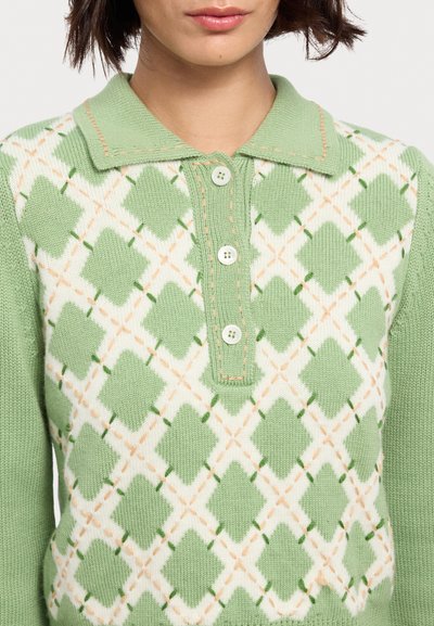 Polo a maglia verde e bianca, con motivo a rombi e accenti arancioni. Quattro bottoni e collo a punta, texture a coste sulle maniche.