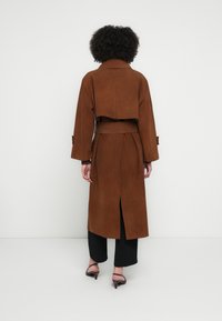 Barna szaru bőr ballonkabát öves derékrésszel, széles ujjakkal és hátsó sliccel. Strukturált gallér és rövidített hát kialakítás jellemzi.