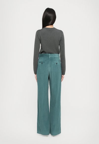 Teal corduroy wide-leg pants with vertical stripes, featuring a high waistband and two back pockets. Styled with a dark gray long-sleeve top.