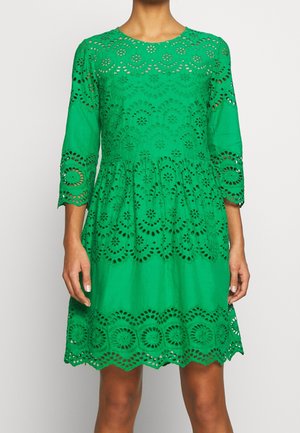Grøn knælængde kjole med bølget kant og indviklede cirkulære udskårne blondenetmønstre på ærmer, krop og kant.