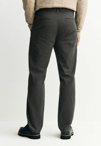 Sötétszürke nadrág egyenes szabással, két hátsó zsebbel és elasztikus derékkal. Fekete lábbelivel párosítva.