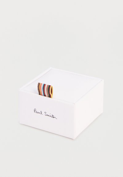 Λευκό τετράγωνο κουτί με την επωνυμία Paul Smith και πολύχρωμο υφασμάτινο λουρί με ρίγες στην κορυφή, σε απλό ανοιχτόχρωμο φόντο.