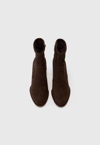 Bottines en suede marron avec un design épuré, bout pointu et fermetures éclair sur les côtés. Texture lisse et accents minimalistes.