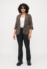 Leopard print blazer made of soft fabric, featuring a relaxed fit and three-quarter sleeves, paired with black slim-fit pants and chunky black shoes.