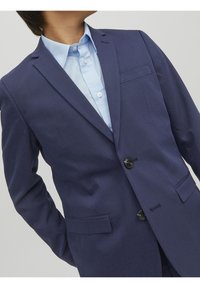 Granatowa marynarka z klapami, z przodem na dwa guziki, kieszeniami bocznymi oraz eleganckim krojem. Jasnoniebieska koszula widoczna pod spodem.