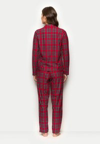 Conjunto de pijama de cuadros rojos con mangas largas y pantalones. El patrón incluye acentos verdes y azules, hecho de una tela suave.