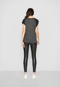 Grå T-skjorte med svarte raglanermer, kombinert med blanke svarte leggings og hvite joggesko, sett fra baksiden. Glatte teksturer er tydelige.