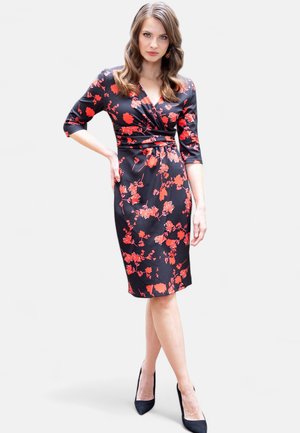 Schwarzes Kleid mit rotem Blumenmuster, figurbetonte Silhouette, V-Ausschnitt, dreiviertel Ärmel und eine gebundene Taillendetail, kombiniert mit schwarzen Absätzen.
