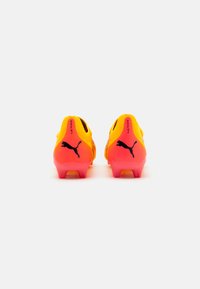 Kollaste ja roosade gradient disainiga jalgpallijalatsid, mille kannal on must Puma logo ja tekstureeritud pealne paremaks haardeks.