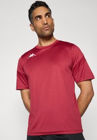 Rode sportieve T-shirt gemaakt van synthetische stof met korte mouwen. Heeft een ronde halslijn en een wit merkembleem op de linkerborst.