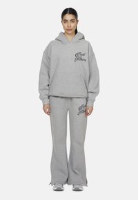 Felpa grigia con cappuccio e pantaloni jogger abbinati, entrambi realizzati in tessuto morbido, con un logo stampato sul davanti, vestibilità comoda e gambe ampie.
