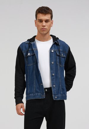 Chaqueta de denim con capucha negra, con un cierre de botones en el frente, dos bolsillos en el pecho y una combinación de colores azul y negro. Ajuste entallado.