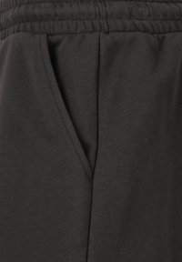 Svarta bomullsbyxor med elastisk midja, sidofickor och en mjuk textur, visade från sidan för att tydligt visa detaljer.