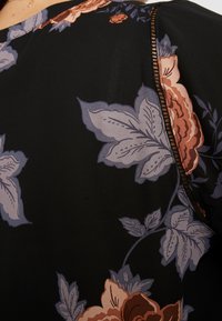 Tessuto nero con motivo floreale colorato. Caratteristiche notevoli: finitura testurizzata, cuciture a contrasto lungo la cucitura e forme variabili delle foglie.