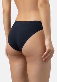 Vrouw in eenvoudige zwarte hooggesneden onderbroek, gezien vanaf de achterkant tegen een witte achtergrond.