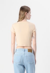 Kort, mouwloos topje in licht perzik ribstof met een ronde halslijn, gecombineerd met lichtblauwe high-waisted jeans met achterzakken.