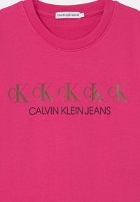 Jasnoróżowy sweatshirt Calvin Klein Jeans z złotymi literami "cK" i czarnym napisem marki na piersi, okrągły dekolt, metka rozmiar 8.