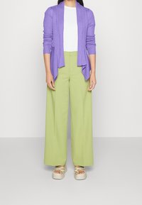 Cardigan violet côtelé, t-shirt blanc, pantalon large vert lime et sandales compensées beige avec des brides vertes.