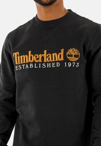 Zwarte sweatshirt van katoenmix, met gouden geborduurd "Timberland" logo met boomicoon en tekst "Established 1973".