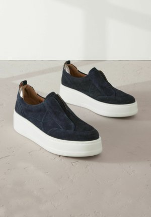 Nachtblaues Wildleder-Slipper mit einer weißen Plateausohle, versehen mit Stichdetails und einem weichen braunen Innenfutter.